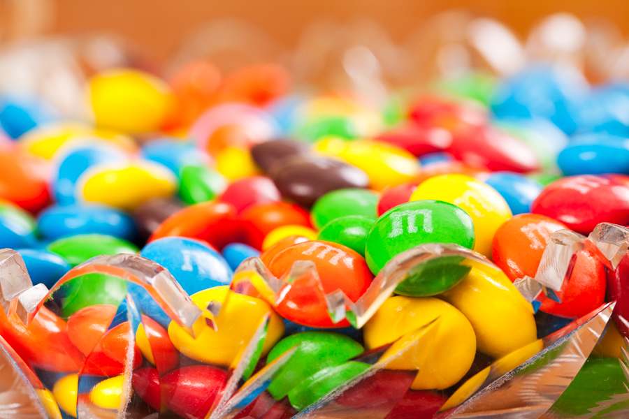 This Brian Charles Steel photograph depicts a brightly let glass dish full of M&Ms. There is a really shallow depth of field.  The M&Ms are arranged so that the colors are well mixed. 